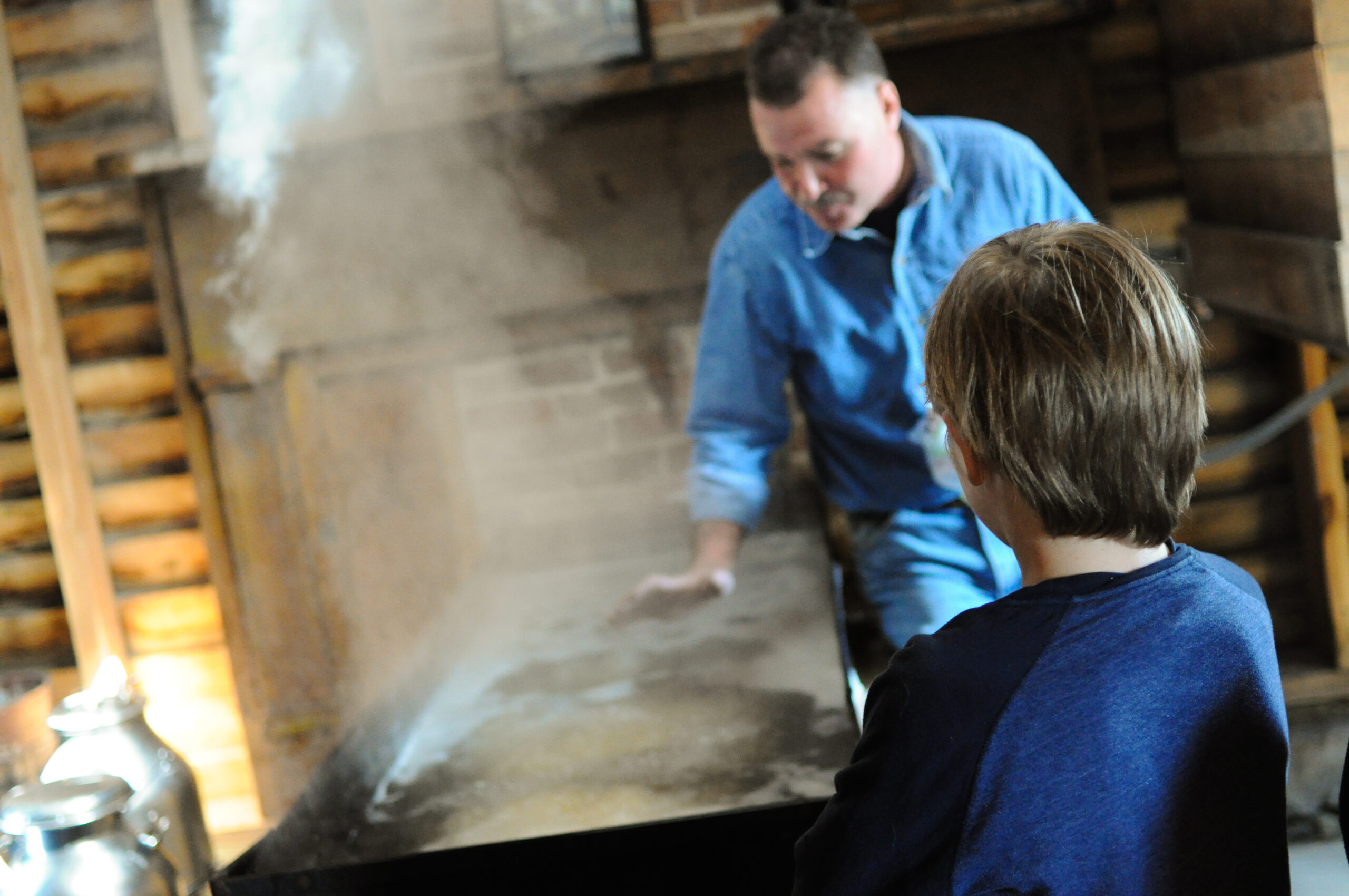 Photo of a man making maple syrup with a child watching.