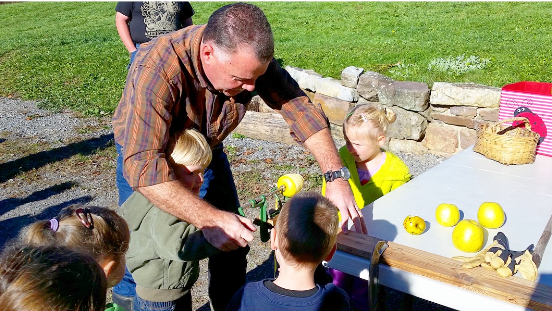 Photo of a man making maple syrup with children watching.